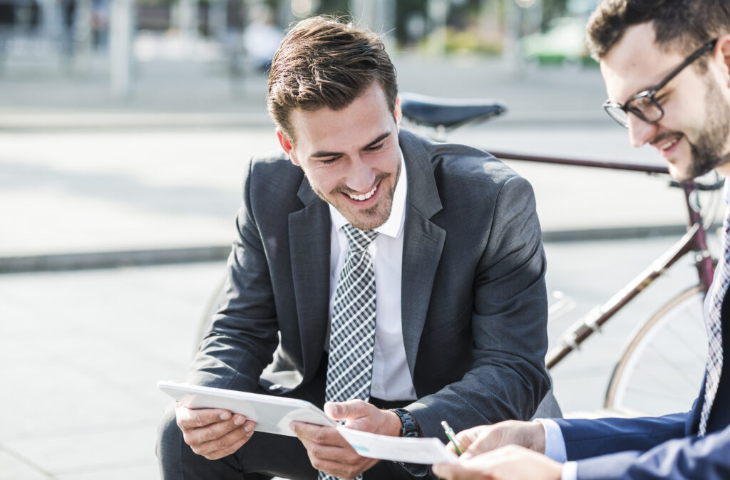 Two young businessmen sitting on bench, discussing files